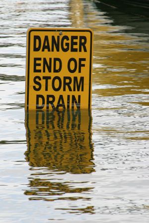 Road sign with "Danger End of Storm Drain" submerged in floodwater.