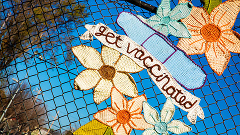 Yarn art on a fence reading "Get vaccinated"