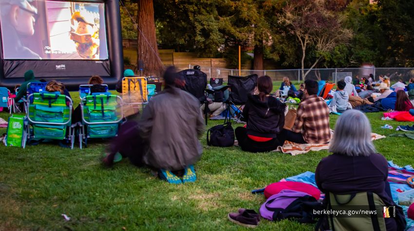 People seated on the ground with blankets and chairs watching outdoor movie