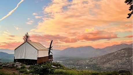 Single tent cabin sits on hillside overlooking a valley with cotton candy sunrise