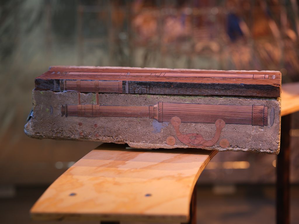 Dark wooden object sits on light wooden bench 