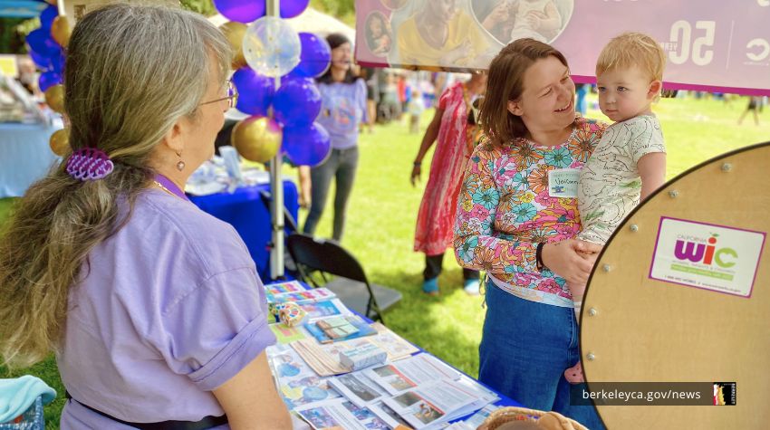 Woman holding a baby speaks with a staff person at a WIC booth