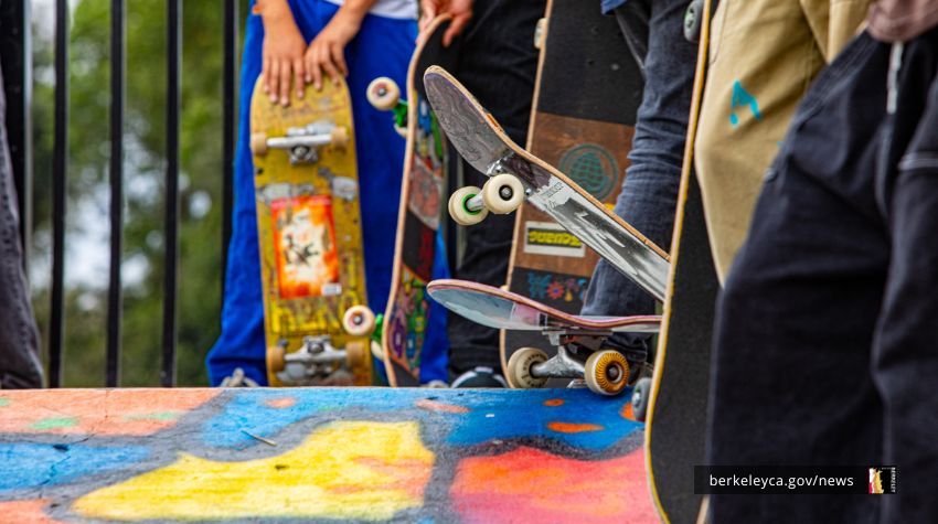 close up of people holding and standing next to skateboards with a colorful mural on the ground.