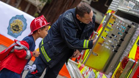 Firefighter shows an engine to a child wearing a firefighter costume