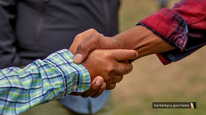 Two people shake hands in an outdoor setting. 