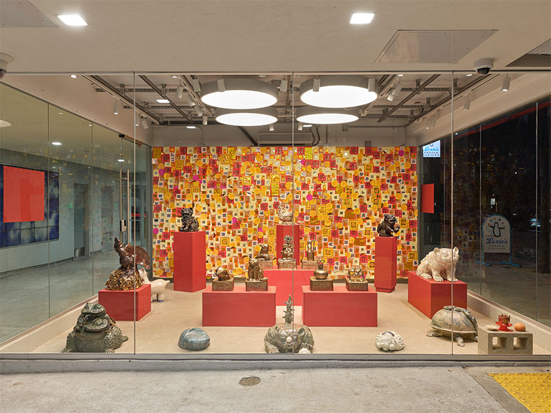 Display of various ceramic animals on pedestals, with back wall covered in small red and yellow pieces of paper