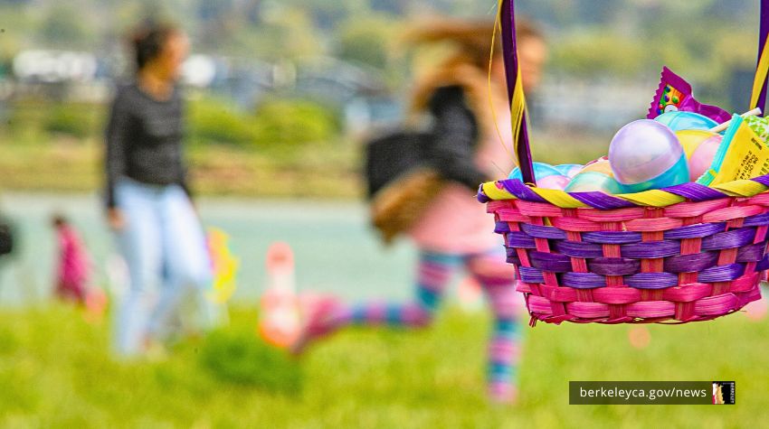 Pink and purple basket is filled with plastic eggs and treats. Children run in the background. 