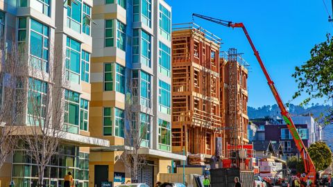 Construction of a multiunit building next to a completed apartment building, with a crane and wood framing visible.