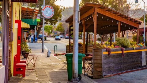 A Berkeley commercial street with storefronts, sidewalk seating, planters, and a covered outdoor dining area.