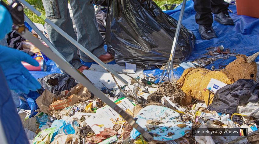 A pile of trash on a blue tarp is being sorted.