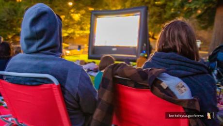 Two people sit in red chairs watching outdoor movie