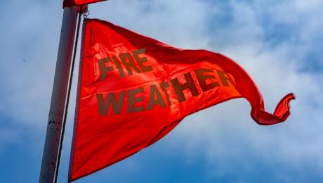 red triangular flag waving in wind with words "fire weather" printed in white text