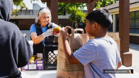 Older woman puts fruit into a young person's paper bag