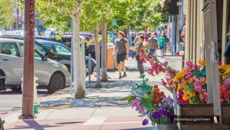 Pedestrians walking on a sidewalk lined by trees and parked cars