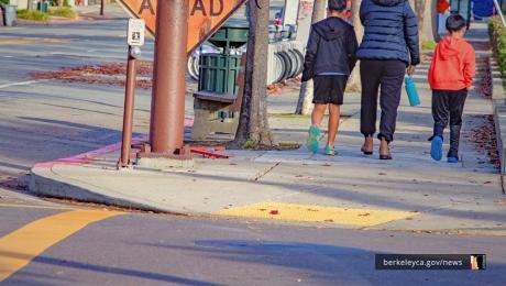 Three pedestrians walk by a street corner on the sidewalk