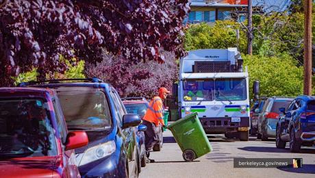 A City of Berkeley trash collection worker moving a compost bin with a trash truck behind