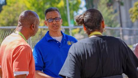 Three adults talk to each other outside. 