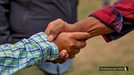 Two people shake hands in an outdoor setting. 