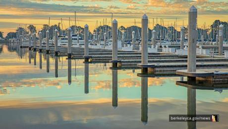 Empty marina docks and sailboat masts line calm water at sunset, with pastel sky colors reflecting across the harbor.