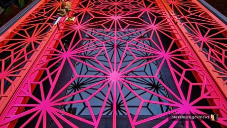 View looking up through a red geometric metal structure with a repeating lattice pattern against the sky.