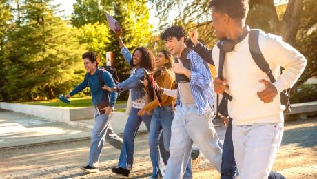 teens walk outside wearing backpacks and talking to each other. 