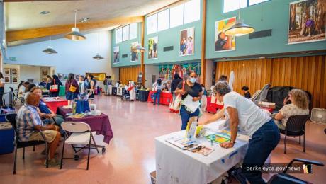 People talk to staff at informational tables in a large room