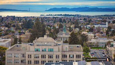 Aerial view with gray building in the foreground and trees and buildings in the background.