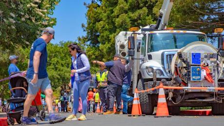 Crowd walks next to large utility vehicle.