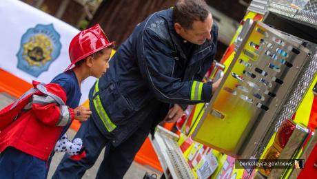 Firefighter shows an engine to a child wearing a firefighter costume