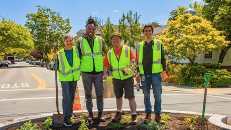 Four volunteers in safety vests pose in a newly planted traffic circle