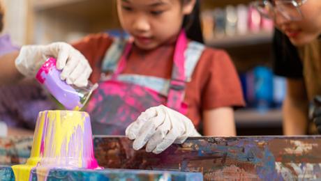 Child painting a colorful pottery piece during an arts and crafts activity.