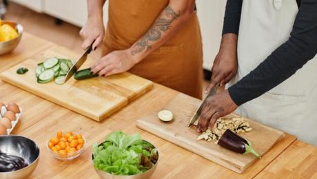 Two people cutting vegetables while cooking together