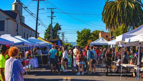 Crowd of people walk around on a street surrounded by tents at a block party.