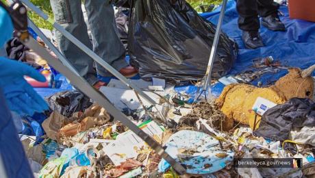 A pile of trash on a blue tarp is being sorted.