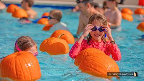 Child swims in an outdoor pool with floating pumpkins in Berkeley, Ca.