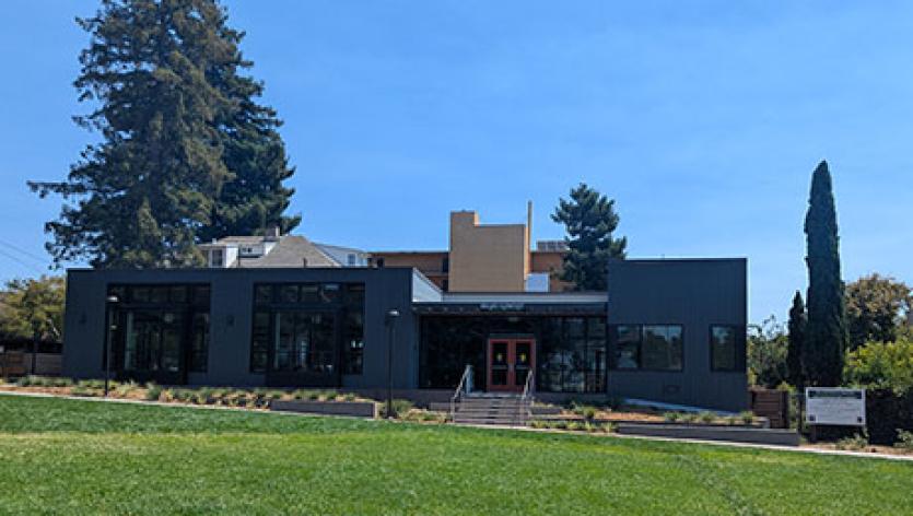 One-story gray building with large windows in a grassy park